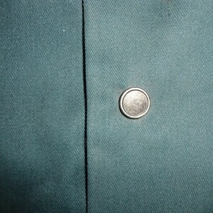 May include: A close-up of a dark teal fabric with a silver button.