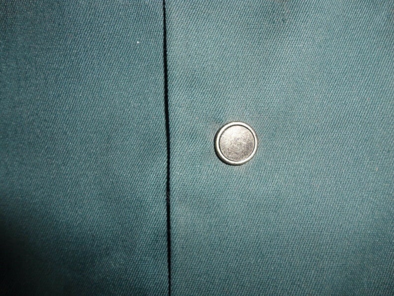 May include: A close-up of a dark teal fabric with a silver button.