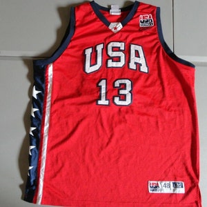 May include: Red basketball jersey with white "USA" and "13" lettering, blue and white star accents on the sides, and a small "USA" tag on the bottom.