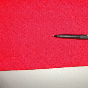 May include: Close-up of a red mesh fabric with a small pen lying on top of it. The pen is black with white lettering that says "uni-ball ON".