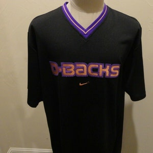 May include: Black short-sleeved t-shirt with a purple and orange "D-backs" logo on the front. The shirt has a purple and white v-neck collar.