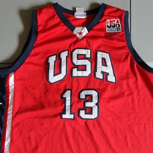 May include: Red basketball jersey with white "USA" and "13" lettering, blue trim, and a small USA Basketball logo on the right shoulder.