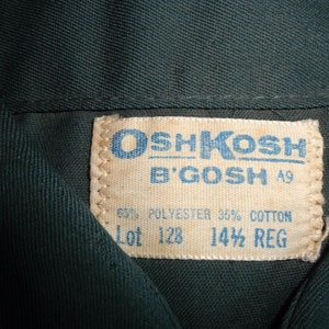 May include: A white tag with blue text that reads "OSHKOSH B'GOSH" and "A9". The tag also says "65% POLYESTER 35% COTTON" and "Lot 128 14 1/2 REG".