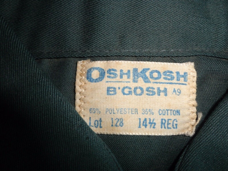 May include: A white tag with blue text that reads "OSHKOSH B'GOSH" and "A9". The tag also says "65% POLYESTER 35% COTTON" and "Lot 128 14 1/2 REG".