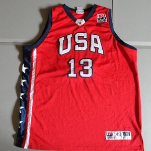 May include: Red basketball jersey with white "USA" and "13" lettering. The jersey has blue and white stars on the side panels and a blue and white "USA" patch on the front.