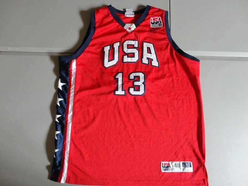May include: Red basketball jersey with white "USA" and "13" lettering. The jersey has blue and white stars on the side panels and a blue and white "USA" patch on the front.