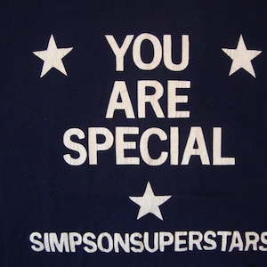 May include: A navy blue t-shirt with white stars and the text "You Are Special" and "Simpsonsuperstars" printed on the front.