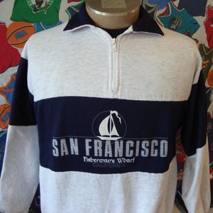 Puede incluir: Una sudadera de manga larga gris y azul marino con un diseño bordado en blanco que dice "SAN FRANCISCO Fisherman's Wharf CALIFORNIA".