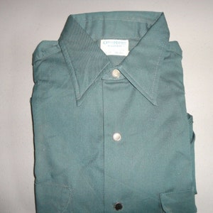 May include: A dark green long-sleeved shirt with a button-down collar and a single pocket on the left side. The shirt has a label that reads "Orion Made in Korea".