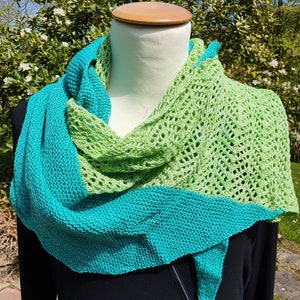 Pode incluir: Uma echarpe de malha verde e azul-turquesa com um padrão de renda. A echarpe está drapeada sobre um manequim.
