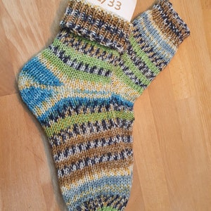 Könnte beinhalten: Ein Paar gestrickte Socken mit einem bunten Muster in Blautönen, Grün, Braun und Weiß. Die Socken haben einen gerippten Bund und sind mit der Größe "32/33" gekennzeichnet.