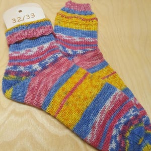 May include: A pair of striped knitted socks in pink, blue and yellow. The socks have a tag attached that says "32/33".