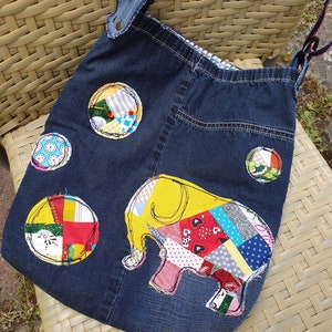 Könnte beinhalten: Eine blaue Jeans-Tragetasche mit einem Patchwork-Elefanten-Design. Der Elefant ist aus bunten Stoffresten gefertigt und hat einen gelben Umriss. Die Tasche hat einen langen Riemen und ist mit anderen bunten Patchwork-Kreisen verziert.