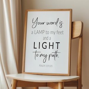 May include: A framed print with a white background and black text. The text reads "Your word is a LAMP to my feet and a LIGHT to my path. PSALM 119:105". The print is sitting on a wooden chair.