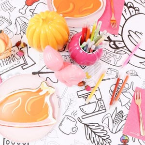 Può includere: Allestimento tavola a tema Ringraziamento con un contenitore a forma di zucca per penne, un oggetto rosa a forma di tacchino e piatti con disegni di tacchino. Include tovaglioli rosa, forchette dorate e una tovaglia da colorare.