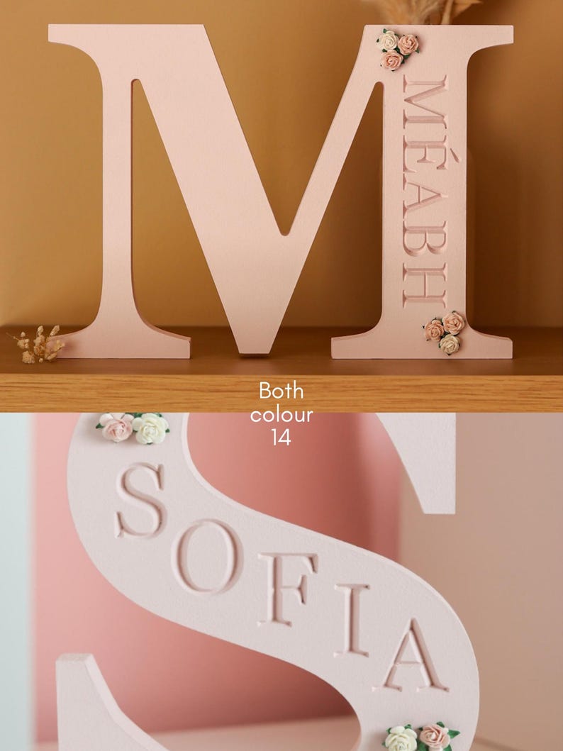 May include: A light pink wooden letter M with the name M&Eacute;ABH engraved vertically and decorated with small fabric flowers, and a light pink wooden letter S with the name SOFIA engraved diagonally and decorated with small fabric flowers.