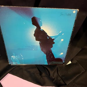 Pu&ograve; includere: Una copertina di un disco in vinile blu e bianco con la silhouette di una persona che suona la chitarra sul palco. La copertina dell'album &egrave; firmata "Jan Gartell".