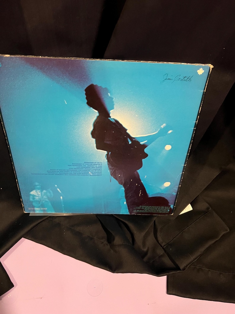 Pu&ograve; includere: Una copertina di un disco in vinile blu e bianco con la silhouette di una persona che suona la chitarra sul palco. La copertina dell'album &egrave; firmata "Jan Gartell".