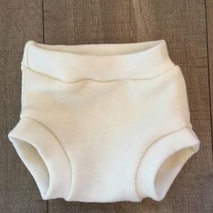 May include: A pair of white cotton baby bloomers with a simple design.
