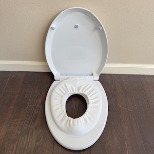 May include: White toilet seat with a white padded insert for a child's potty training.