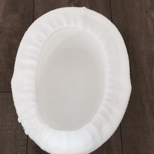 May include: A white, oval-shaped pet bed with a plush, cushioned rim. The bed's interior is a smooth, solid white, providing a comfortable space for small pets. The bed is designed for comfort and relaxation.