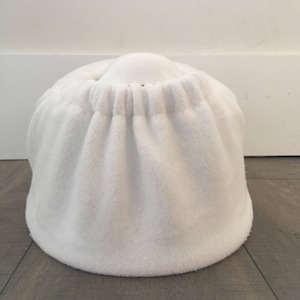 May include: White plush toilet seat cover with a white ceramic toilet bowl underneath.