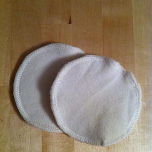 May include: Two white cotton nursing pads with a stitched edge.
