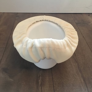 May include: A white toilet seat cover made of soft, plush fabric. The cover is designed to fit over a standard toilet seat and provides a comfortable and hygienic surface.