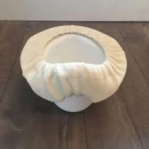May include: A white toilet bowl seat cover made of soft, plush fabric. The cover is designed to fit over the toilet bowl seat and provide a comfortable and hygienic surface.