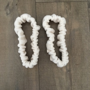May include: Two white fabric hair scrunchies with a ruffled texture.