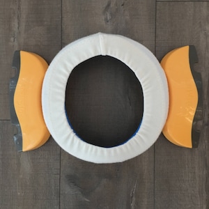 May include: A white padded toilet seat ring with two yellow and black side supports. The supports have the word "Potty" printed on them.