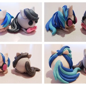 May include: A pair of handmade clay unicorn figurines. One unicorn has blue and white hair with pink headphones, the other has black hair. Both have pink bow ties and are lying down.