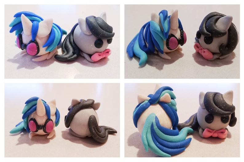 May include: A pair of handmade clay unicorn figurines. One unicorn has blue and white hair with pink headphones, the other has black hair. Both have pink bow ties and are lying down.