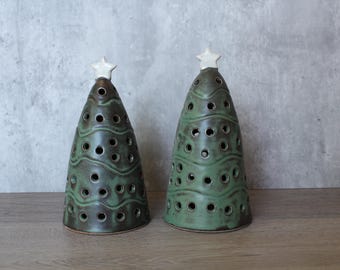 May include: Two cone-shaped ceramic sculptures in the form of Christmas trees. Each piece features a dark green glaze with brown undertones, wavy horizontal lines, and numerous circular cutouts. A small white star sits atop each ceramic tree.