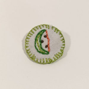 May include: Embroidered patch with a watermelon slice design. The patch has a white background and a green stitched border. The watermelon slice is green and orange with brown seeds.