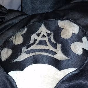 Puede incluir: Vestido de satén negro con una superposición de encaje blanco que presenta un diseño geométrico. La superposición de encaje tiene forma de corazón.