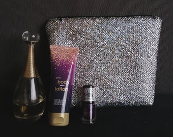 May include: A silver glitter cosmetic bag with a purple and gold glitter body lotion tube, a clear glass bottle of perfume, and a small bottle of purple glitter nail polish. The nail polish bottle has the text "Show Stopper" on it. The lotion tube has the text "glitter body lotion" and "warm & velvety with glitter & natural oils".