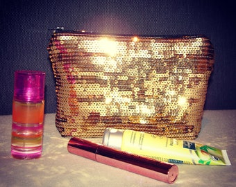 May include: A gold sequined makeup bag, a clear bottle with pink and orange liquid, a pink and gold mascara tube, and a yellow tube of hand cream with the text "Avocado Oil" on the label.