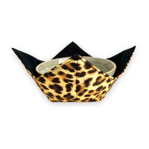 May include: A leopard print bowl cozy with black trim. The cozy is designed to fit a small bowl and keep it warm.