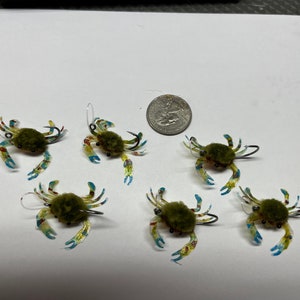 May include: Six green, blue and yellow crab-shaped fishing lures with fuzzy green bodies and silver hooks.