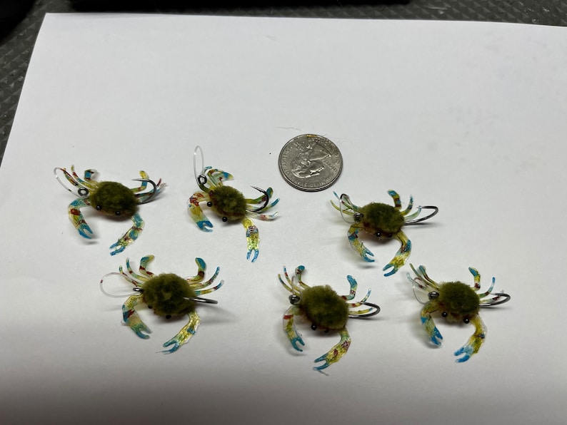 May include: Six green, blue and yellow crab-shaped fishing lures with fuzzy green bodies and silver hooks.