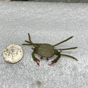 May include: A green and red crab pin with a safety pin closure. The crab is made of felt and has a textured surface.