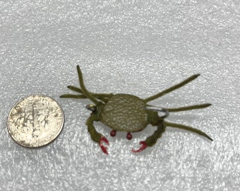 May include: A green and red crab pin with a safety pin fastening. The crab is made of felt and has a textured surface.