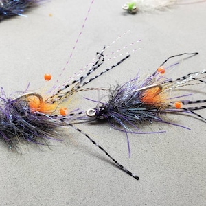 May include: Two purple and black fly fishing lures with orange beads and white feathers.