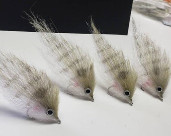 May include: Four fishing flies, each with a light brown and white body, silver hook, and black eye. The flies are designed to resemble small fish, with a feathery texture, ideal for fly fishing.
