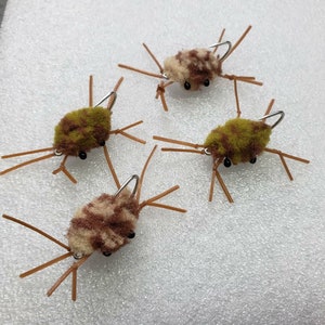 May include: Four brown and green fuzzy fly fishing lures with brown legs and silver hooks.