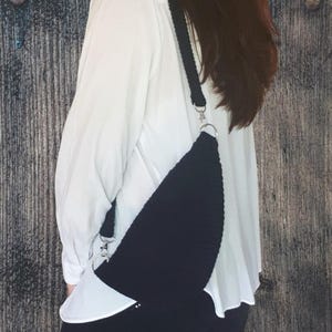 Puede incluir: Un bolso bandolera de crochet negro con una cadena plateada. El bolso se lleva sobre una camisa blanca.