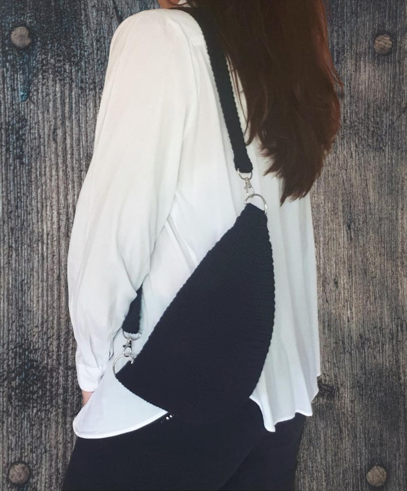 Puede incluir: Un bolso bandolera de crochet negro con una cadena plateada. El bolso se lleva sobre una camisa blanca.