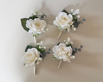 May include: Four white rose boutonnieres with greenery and small white flowers.