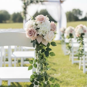 Può includere: Sedie bianche decorate con composizioni floreali di rose rosa e bianche e verde, allestite per una cerimonia nuziale all'aperto. I fiori sono attaccati alle sedie con foglie verdi.